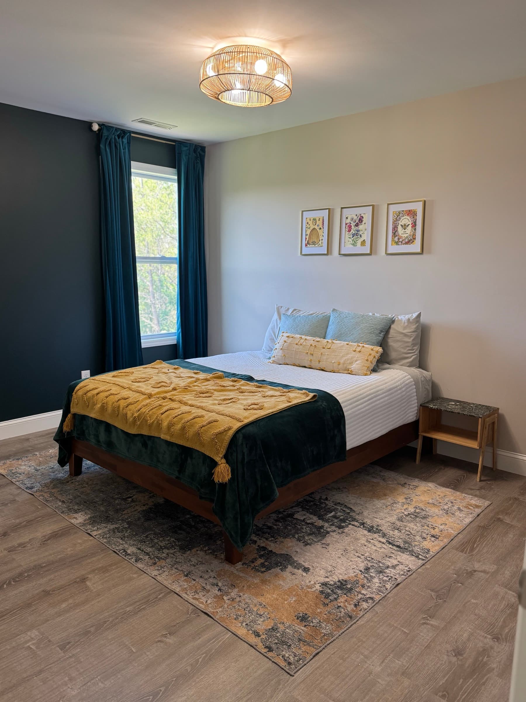 Bedroom with teal accents, layered bedding, and forest view window