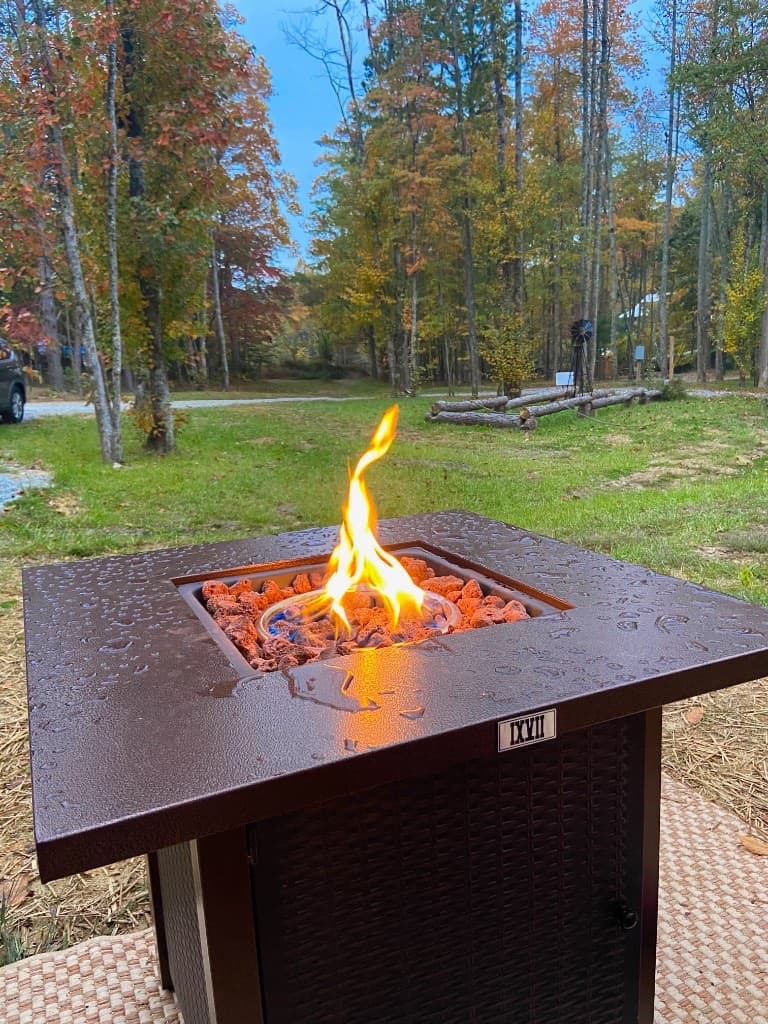 Gas fire pit with flame against autumn trees
