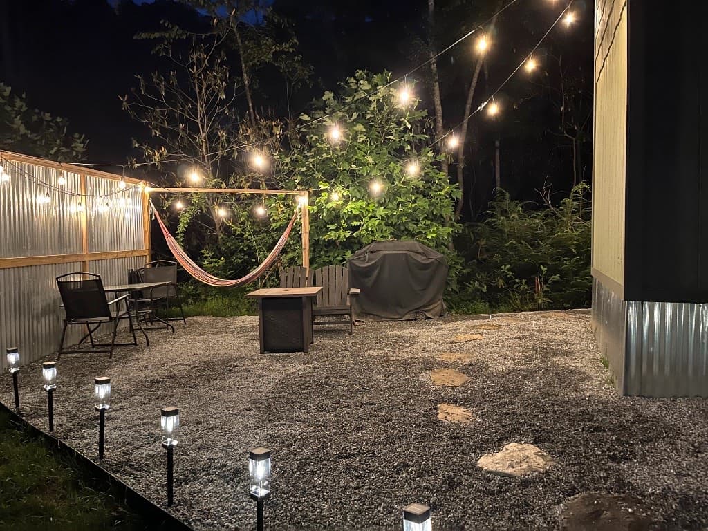 Night patio with fire pit, hammock, Adirondack chairs, and string lights